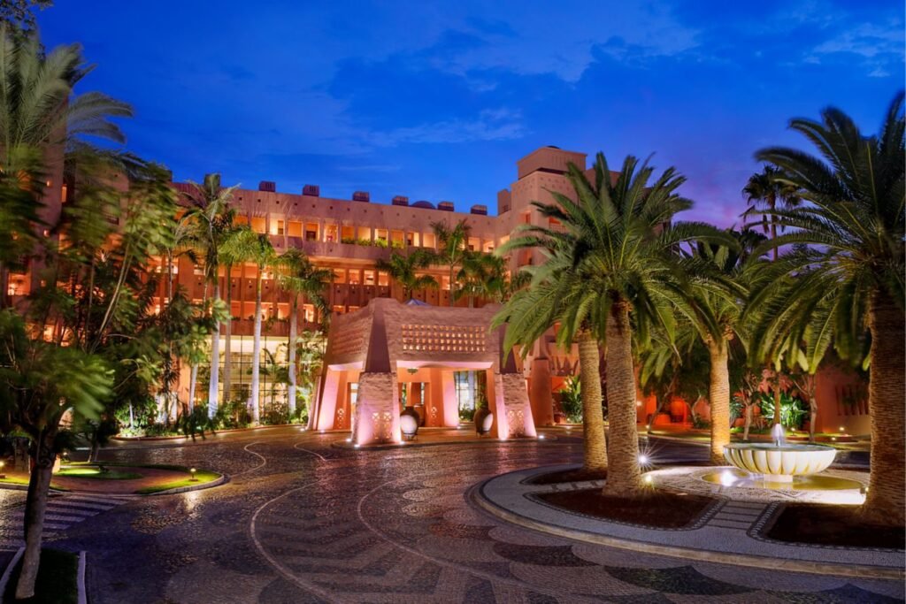 A palm-lined resort entrance and illuminated courtyard at dusk