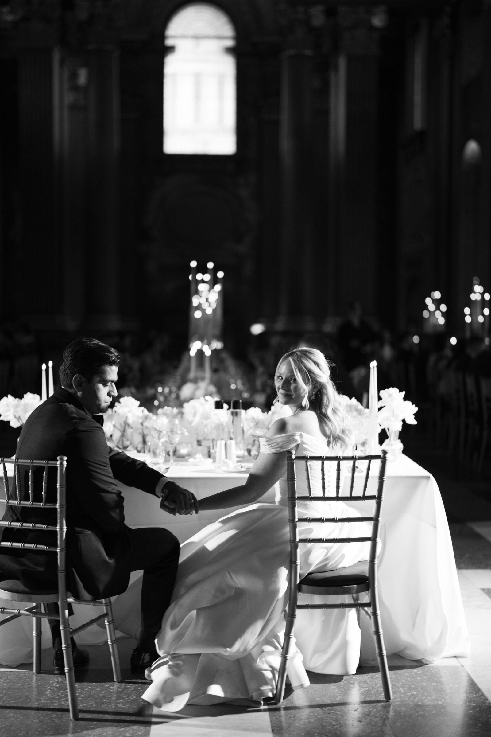 Black and white London wedding reception design inside an ornate historic hall with candlelight and long dining tables.