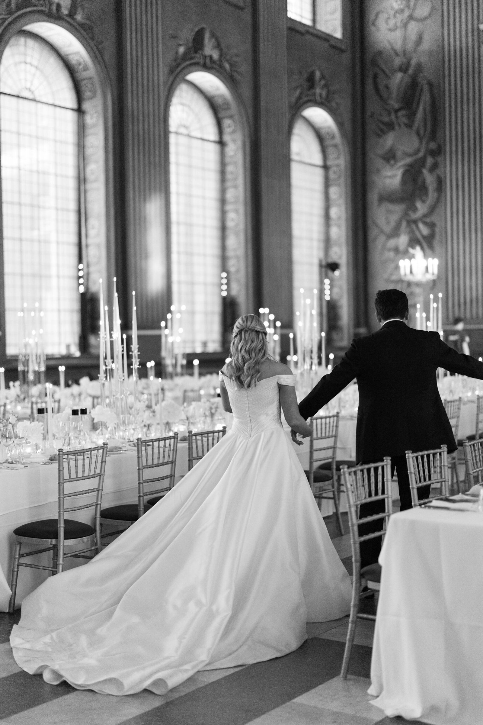 Black and white London wedding reception design inside an ornate historic hall with candlelight and long dining tables.