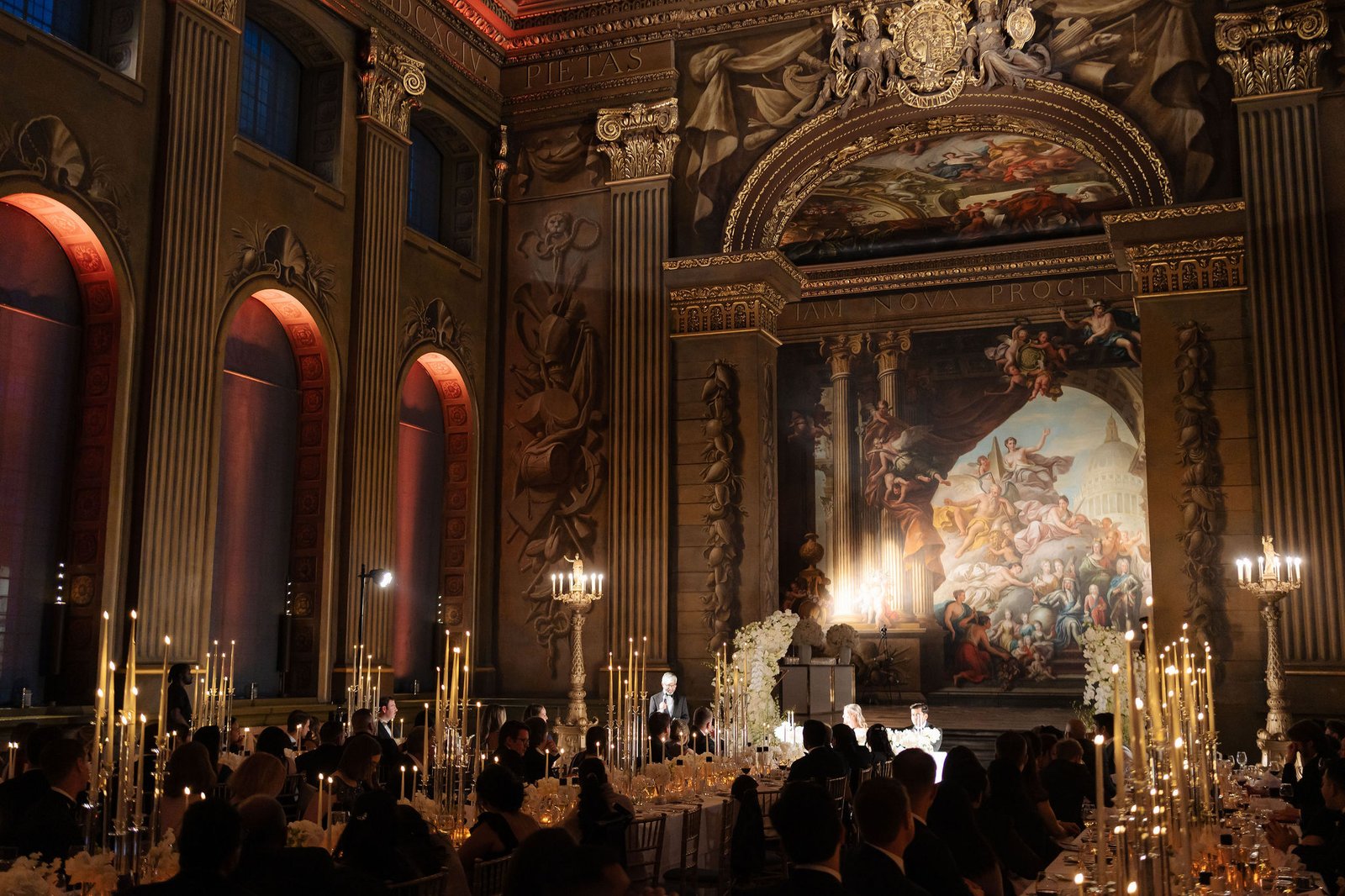 London wedding reception design inside an ornate historic hall with candlelight and long dining tables.