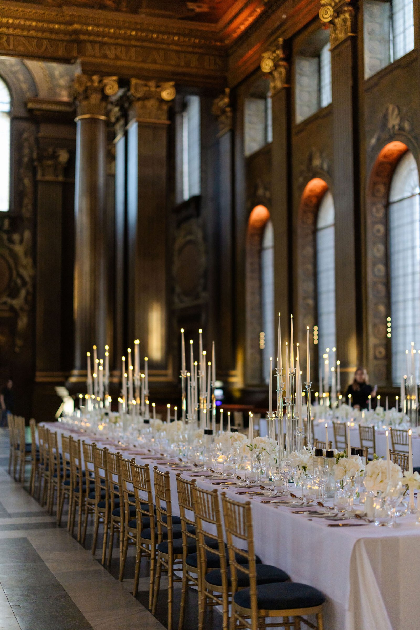 London wedding reception design inside an ornate historic hall with candlelight and long dining tables.