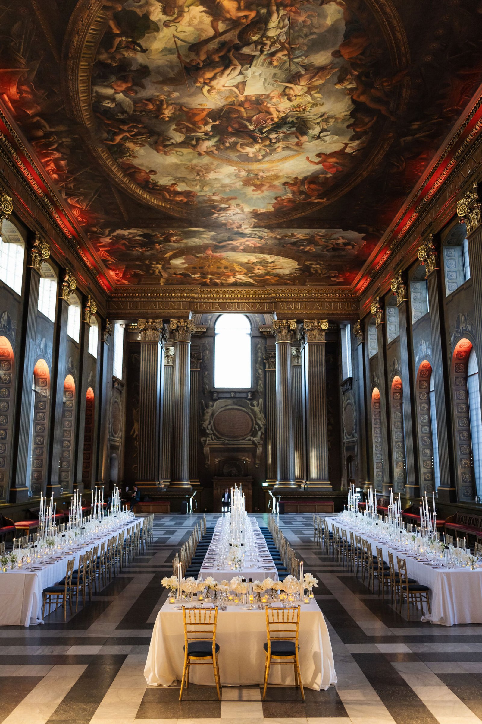 London wedding reception design inside an ornate historic hall with candlelight and long dining tables.